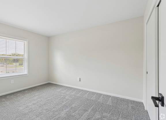 A room with a carpeted floor and a window with blinds.