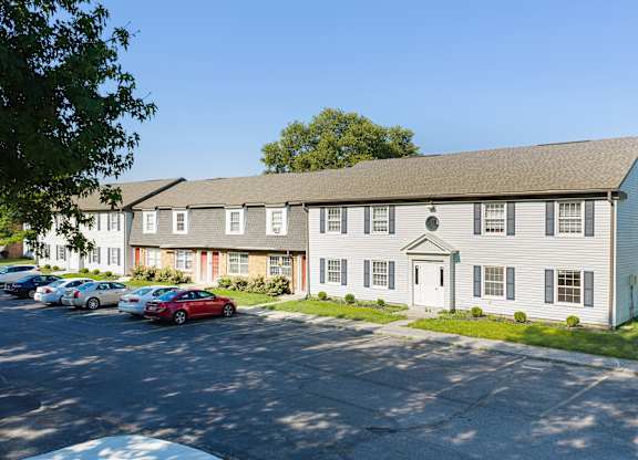 A white building with a grey roof and a parking lot in front.
