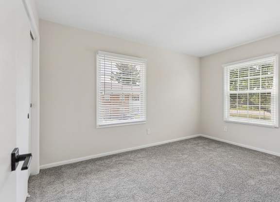 A room with two windows and carpeted floor.