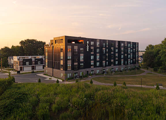 A modern building with a dark facade stands in the foreground with a sunset sky in the background.