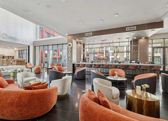 A modern lounge area with orange chairs and a bar in the background.