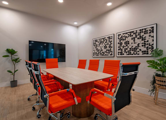 A conference room with a long table and orange chairs.