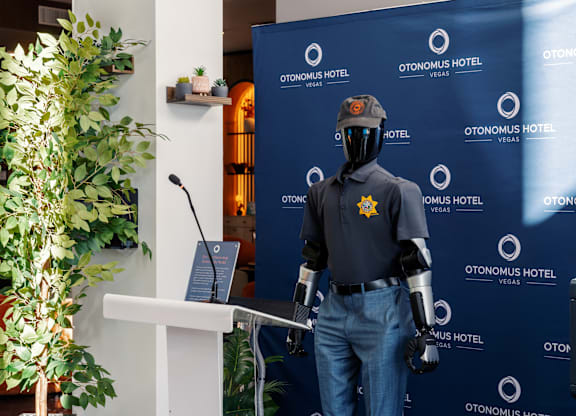A mannequin dressed in a police uniform stands in front of a backdrop for Otonomus Hotel.