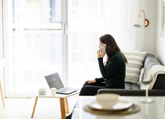 A woman is sitting on a couch with a laptop and a cup of coffee on the table in front of her.