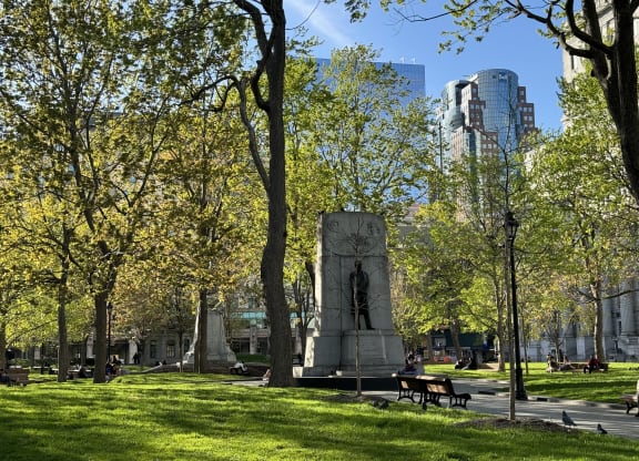 a statue in a park with trees and a city in the background