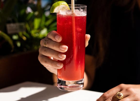 a woman holding a red cocktail in a glass with a straw