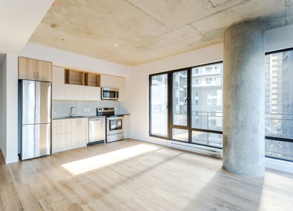 an empty living room with a kitchen and a large window