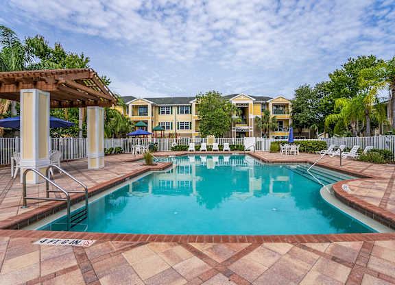 A large swimming pool surrounded by a tiled patio and lounge chairs.