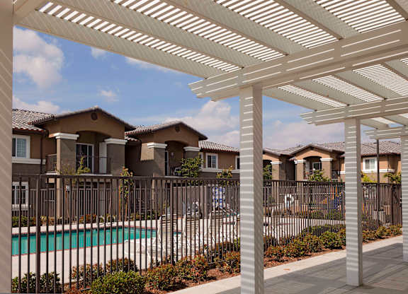 a white pergola sits in front of a pool with apartment buildings in the background