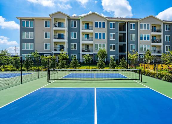 A tennis court in front of a large apartment building.