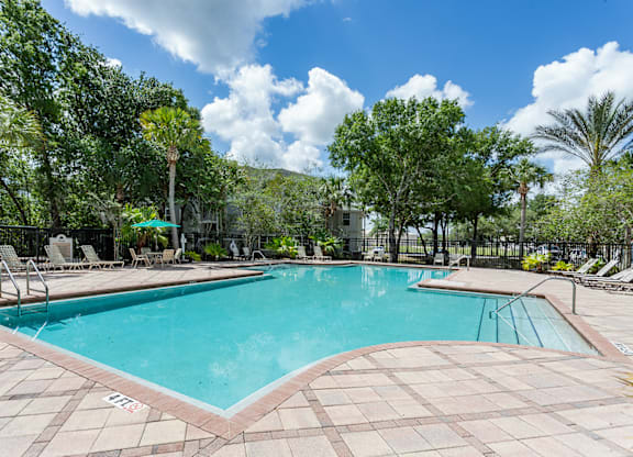 A large swimming pool surrounded by trees and lounge chairs.