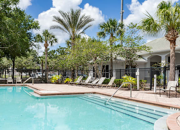 A pool surrounded by palm trees and lounge chairs.
