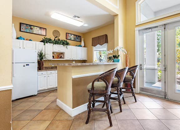 A kitchen with a white refrigerator and brown chairs.