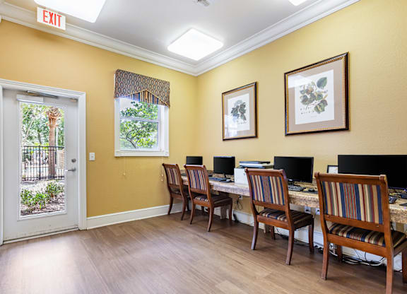 A room with yellow walls has a desk with two computers and two chairs.