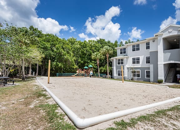 A sandy area in front of a building with trees in the background.