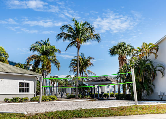 A white building with a green awning is surrounded by palm trees.
