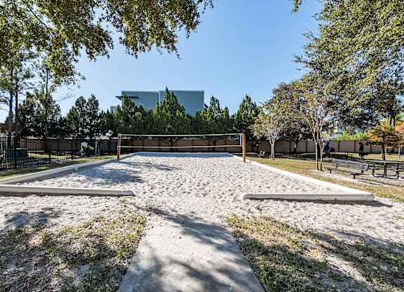 A playground with a sandbox in the foreground and a building in the background.