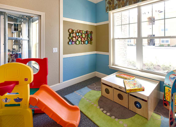 A child's playroom with a yellow chair, a red slide, and a brown and green play mat.