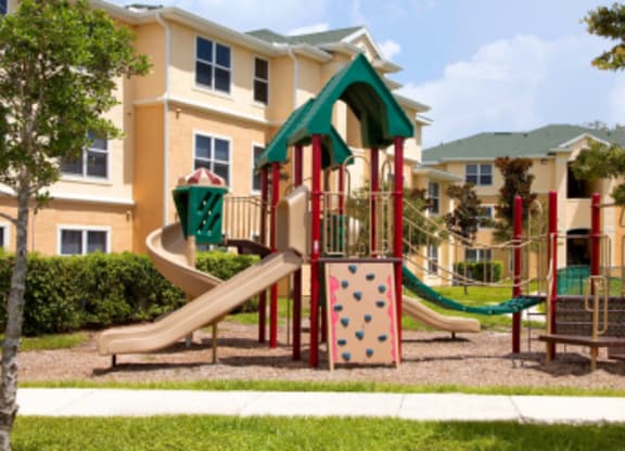 A playground with a slide and a climbing frame in front of a building.