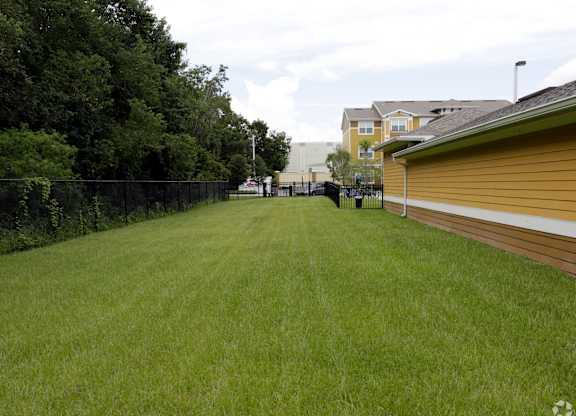 A grassy field with a fence and houses in the background.