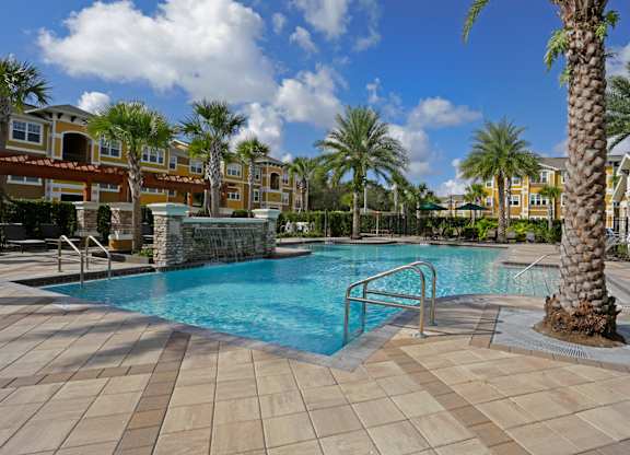 A pool surrounded by palm trees and a building in the background.