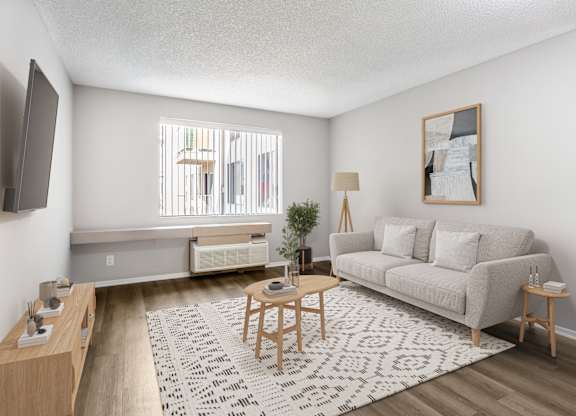 A living room with a grey couch, a wooden table, and a television on the wall.