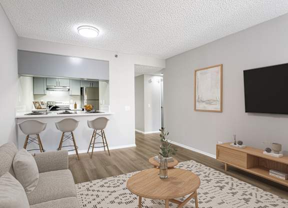 A living room with a grey couch, a wooden coffee table, and a kitchen area in the background.