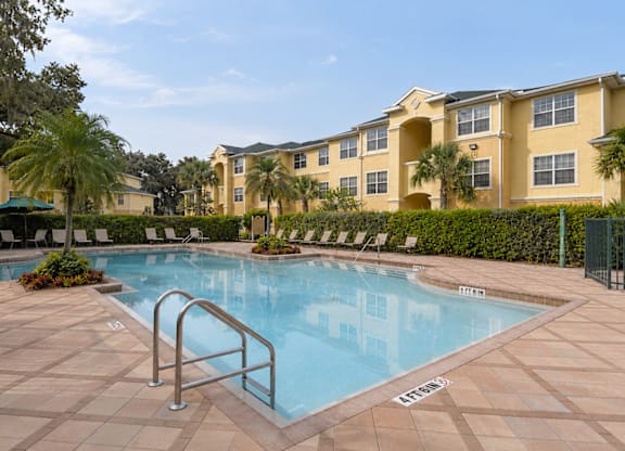 A pool surrounded by a tiled patio and a building in the background.