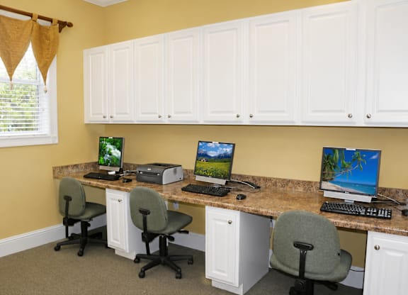 A home office with a yellow wall and a desk with two computers and two chairs.