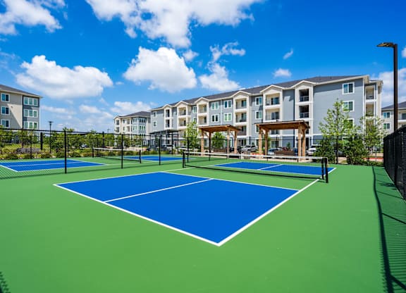 A tennis court with a blue surface and white lines is surrounded by a black fence.