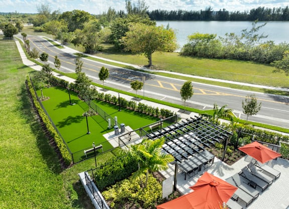 A road with a grassy median and a patio with red umbrellas.