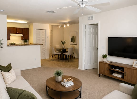 A living room with a white couch, a coffee table, a television, and a dining area in the background.
