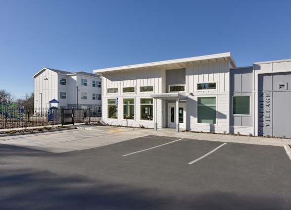 A white building with a grey roof and a parking lot in front.