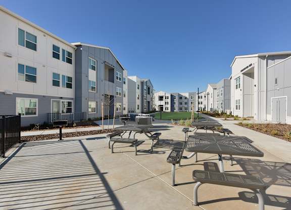A sunny day at a modern apartment complex with a picnic table and benches in the foreground.