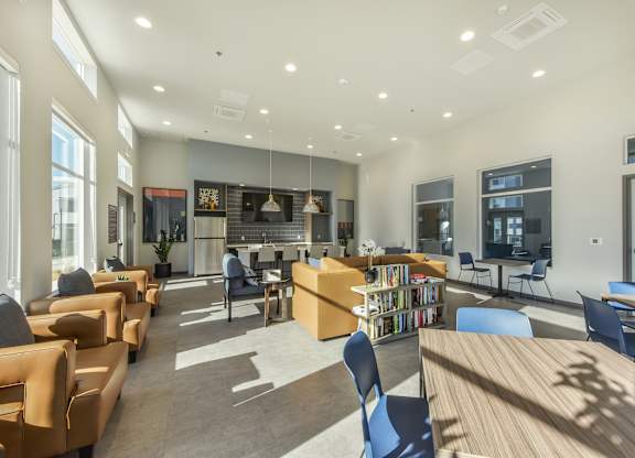 A spacious library with wooden tables and chairs, a bookshelf, and a large window.