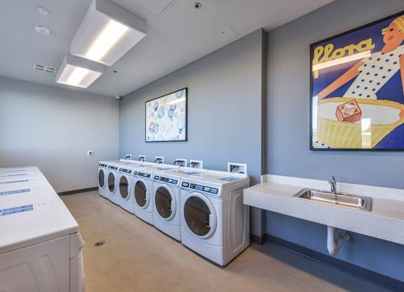A laundry room with a row of washing machines and a sink.
