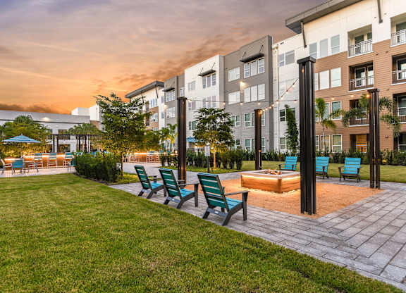 A sunset view of a modern apartment complex with a pool and lounge chairs.
