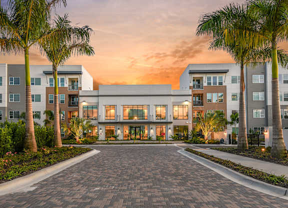 A modern building with a driveway and palm trees in front.