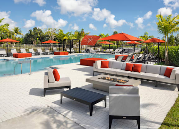 A poolside seating area with red umbrellas and white couches.