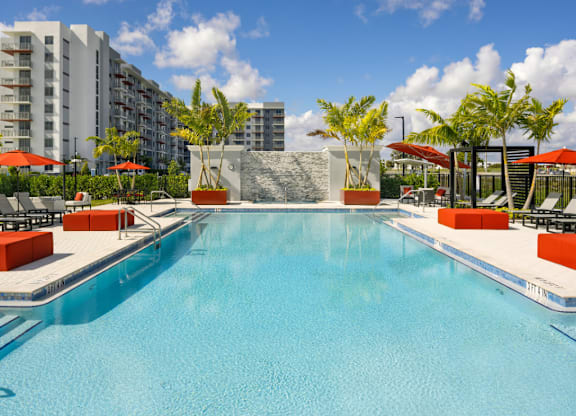 A large swimming pool with a red umbrella and a building in the background.