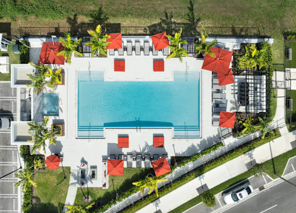 An aerial view of a pool surrounded by red umbrellas and white buildings.