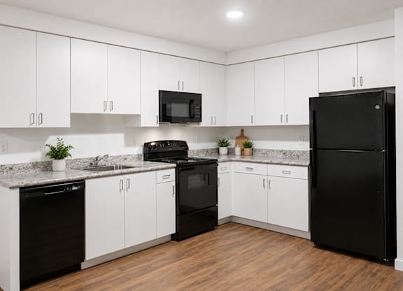 A black refrigerator stands in a kitchen with white cabinets and a granite countertop.