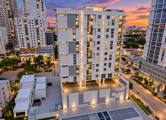 A modern white building with a glass facade is illuminated at dusk.