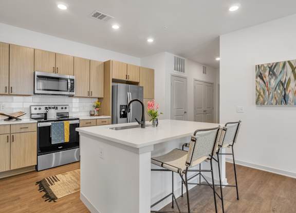 a kitchen with a large island with a white counter top and three chairs