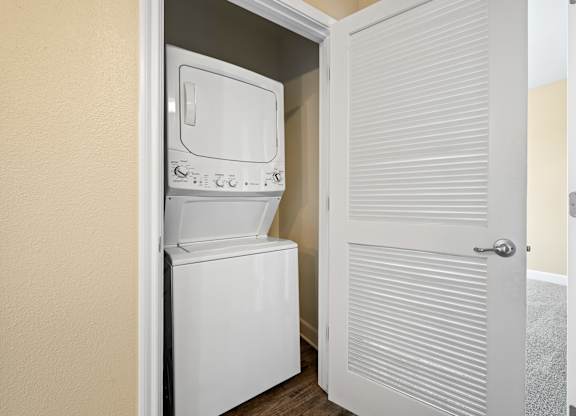 A white stackable washer and dryer is installed in a narrow space between two walls.