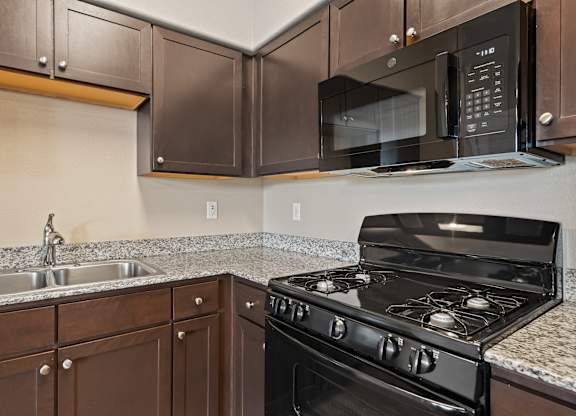 A black microwave is mounted above a black stove in a kitchen.