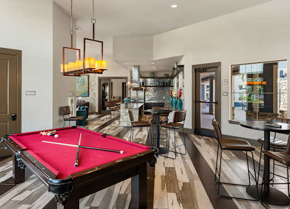 A pool table is in the middle of a room with a bar and chairs.