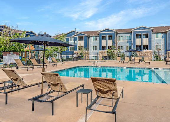 A pool area with chairs and umbrellas in front of apartment buildings.