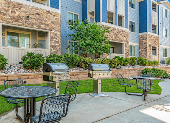 A patio with a table, chairs, and two grills in front of a building.