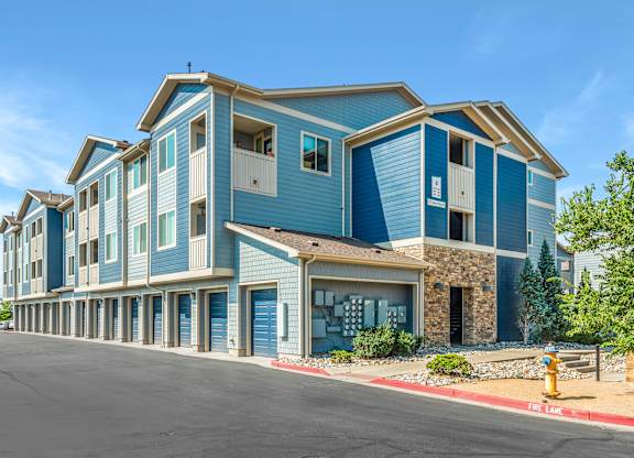 A blue and white apartment building with a parking lot in front.